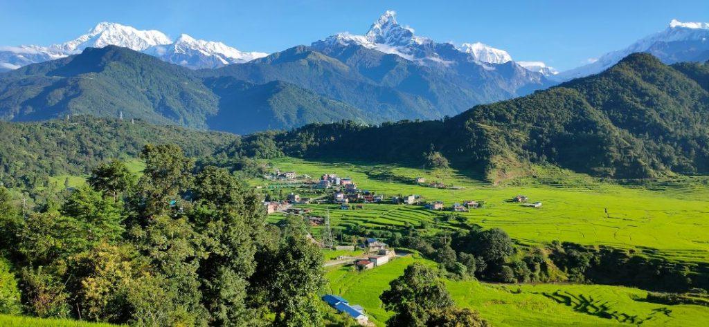 Pokhara, Nepal with lush green hills in the foreground and the Himalayan mountain range visible in the background under a clear sky. (image chosen for Lakeside vs Sarangkot blog)