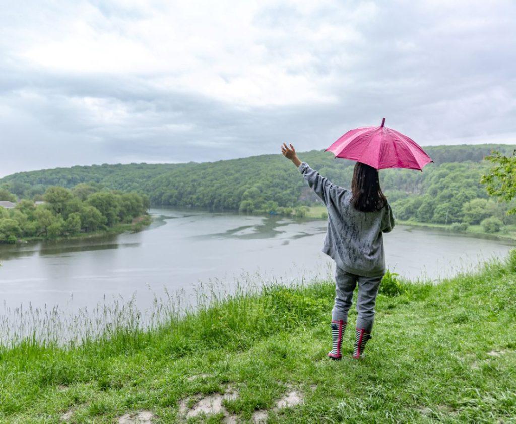 Person standing with an umbrella on a grassy hill overlooking a lake in Pokhara during rainy weather, illustrating common mistakes visitors make in Pokhara when visiting during monsoon season.
