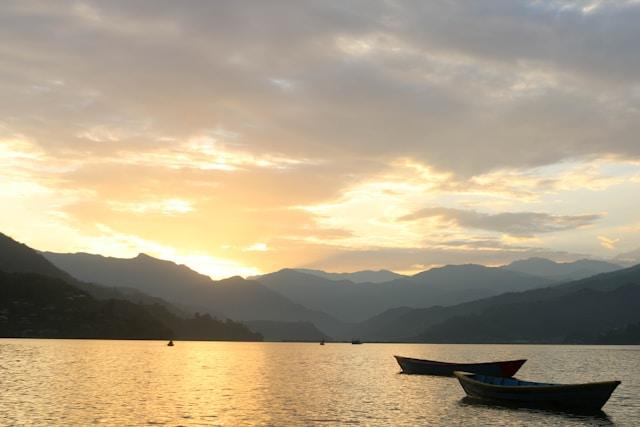 Sunset view over Pokhara Lake with mountains and boat silhouettes